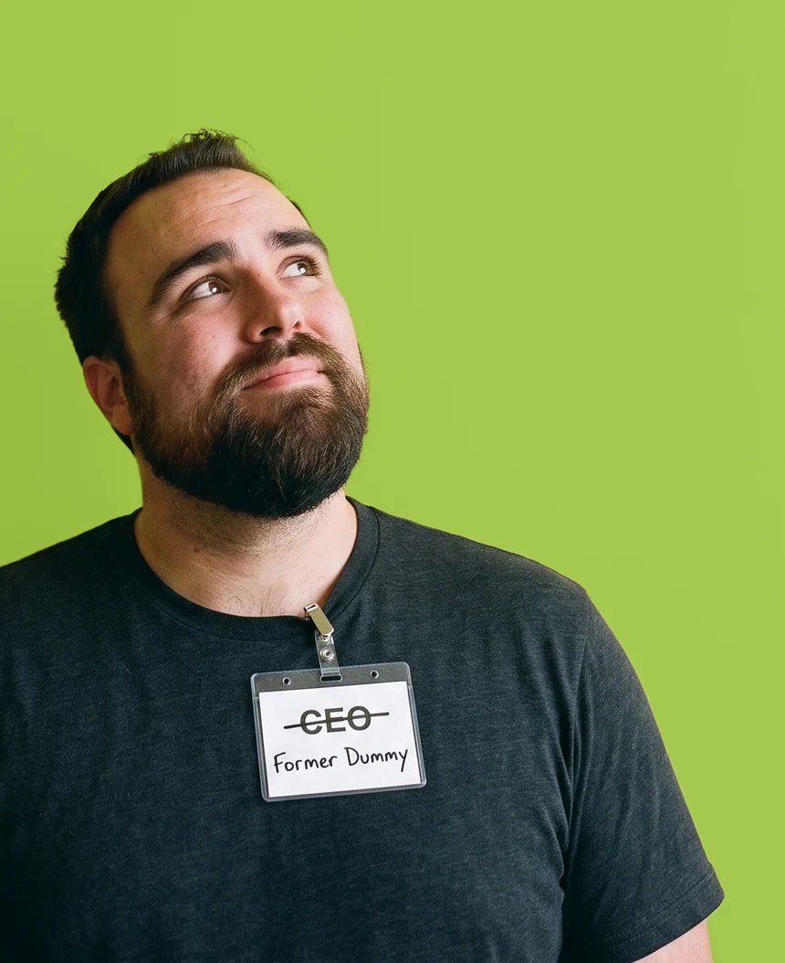 JJ Reynolds against a lime wall, looking up at the title, wearing a conference badge with CEO crossed out and Former Dummy written underneath