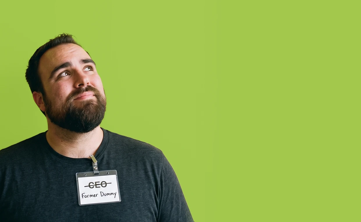 JJ Reynolds against a lime wall, looking up at the title, wearing a conference badge with CEO crossed out and Former Dummy written underneath